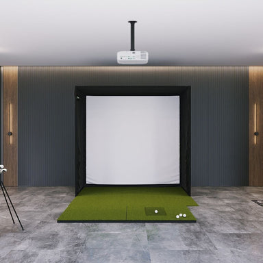 Indoor golf simulator setup with green mat and white screen on a gray floor.