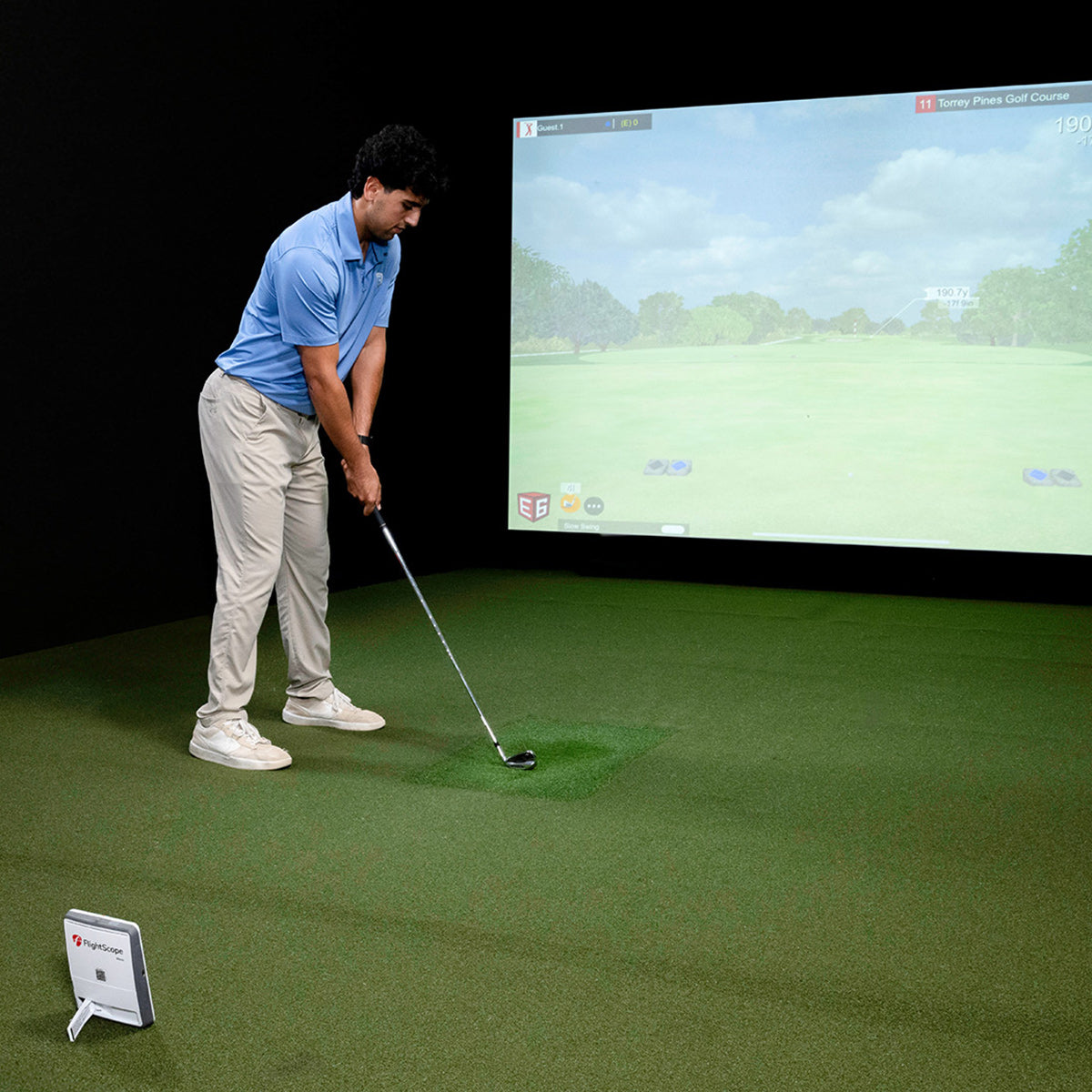 Person playing virtual golf in a simulator with a screen displaying a golf course.