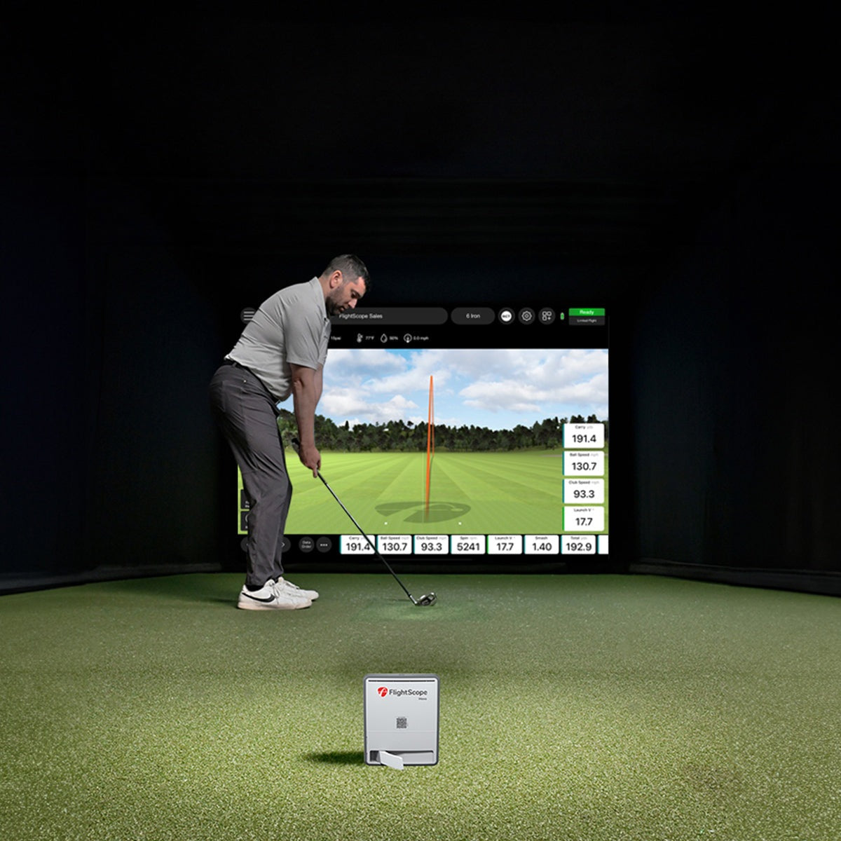 Man practicing golf swings in a simulator room with a screen displaying a golf course.