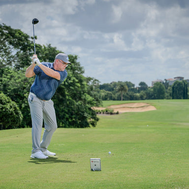 Man playing golf on a green course with trees and sky in the background