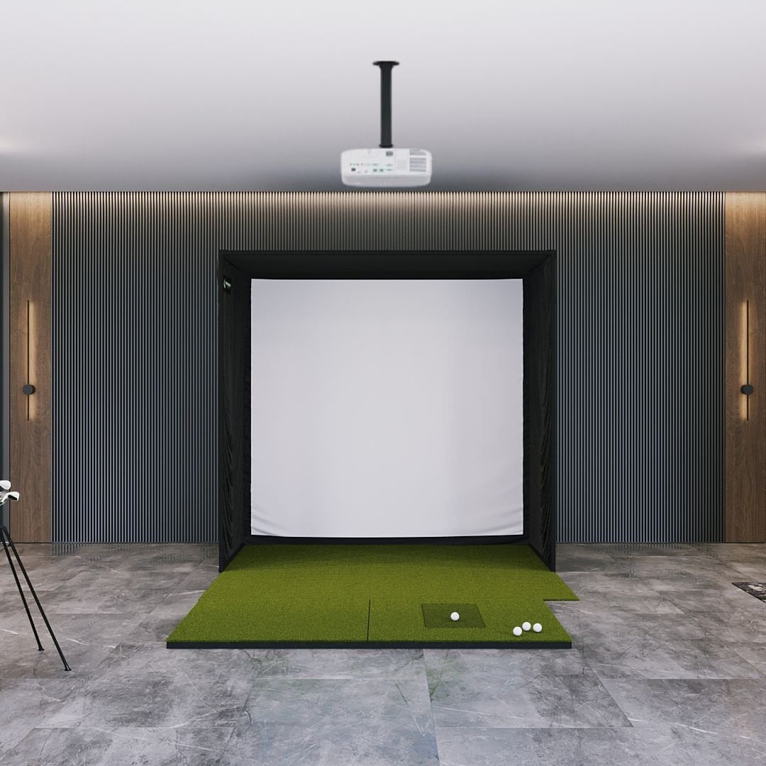 Indoor golf simulator setup with green mat and white screen on a gray floor.