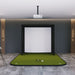Golf practice simulator with green mat and white screen in a room with wooden walls.